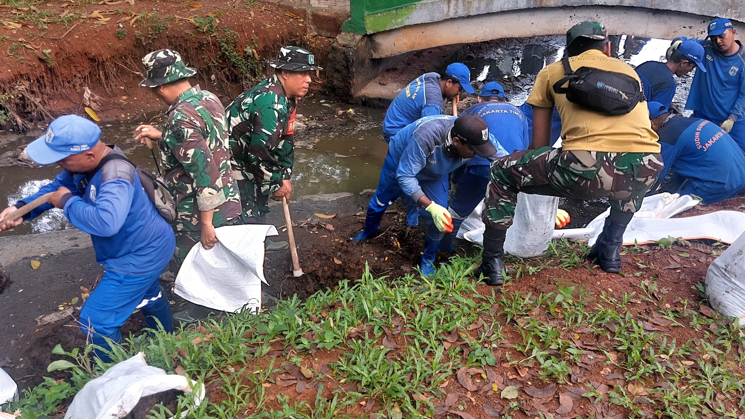 Kolaborasi Babinsa Kelurahan Lubang Buaya Bersama Petugas Dinas Tata Air Bersihkan Saluran Air